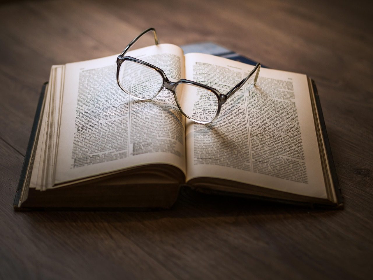 Reading glasses resting on an open book with soft lighting.
